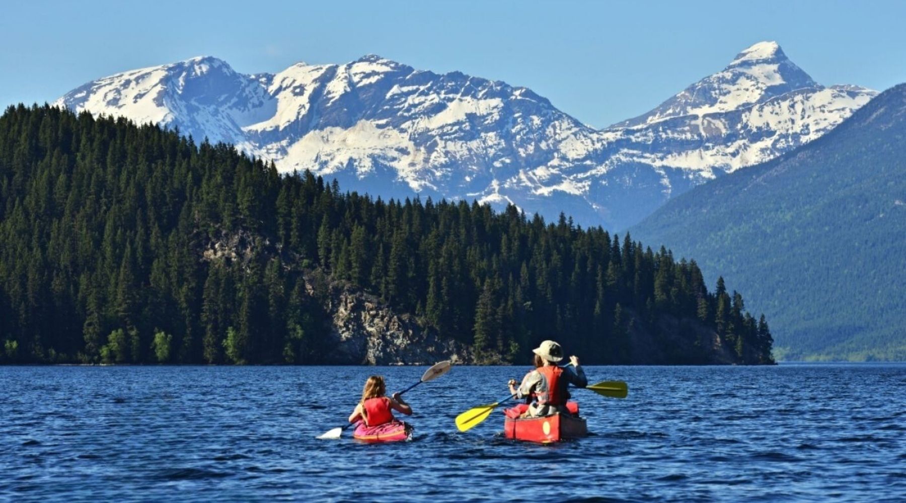 Two adventurers enjoying a 5-day all-inclusive canoe and hike combination trip on the tranquil Clearwater lake, with a scenic mountain backdrop